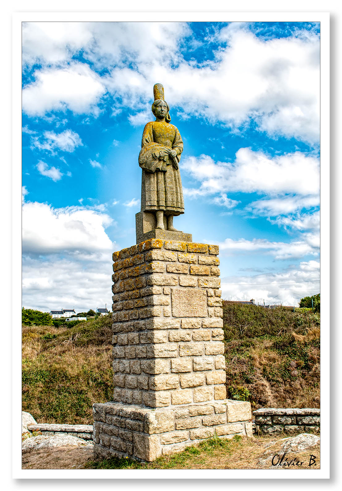 Statue Bigouden en granit surplombant le port de Pors-Poullan, face à l'océan sous un ciel bleu