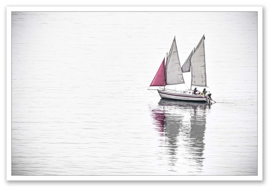 Navire de plaisance avançant paisiblement sur une mer calme sous des voiles et un foc rouge, image minimaliste